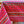 Colorful patterned tablecloth with a red background and stripes of olive sprigs, floral designs, vines, and french medallions on a wooden surface.