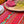 Bright red tablecloth with  pattern of olive sprigs, flowers and french medallions. A wicker tray on top of tablecloth holding red and blue matching napkins and green wine glasses.