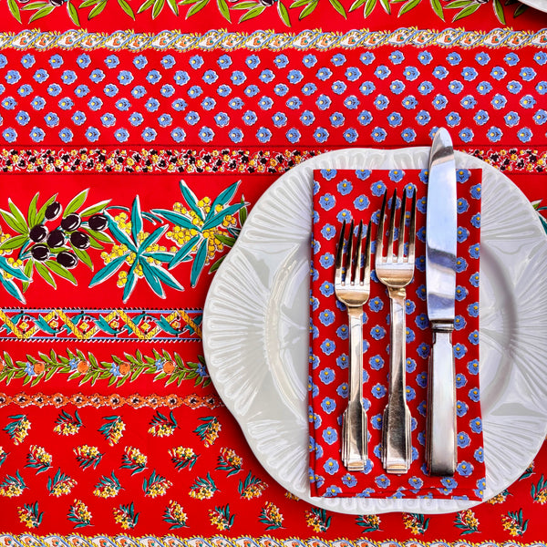 Set table with white plates, silverware, and a red patterned tablecloth.